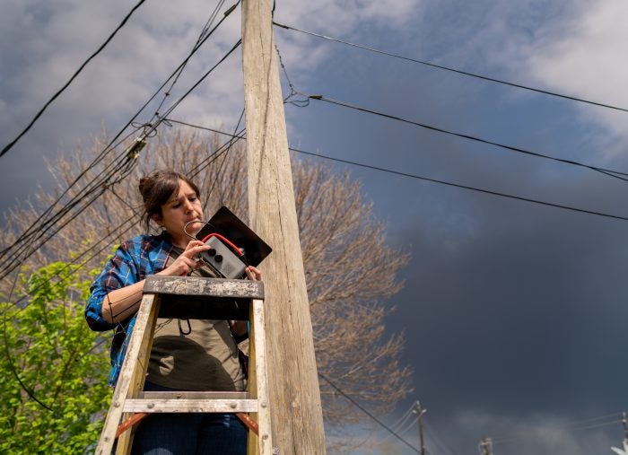 A woman standing on ladder, Installing a low-cost hyperlocal air quality monitor